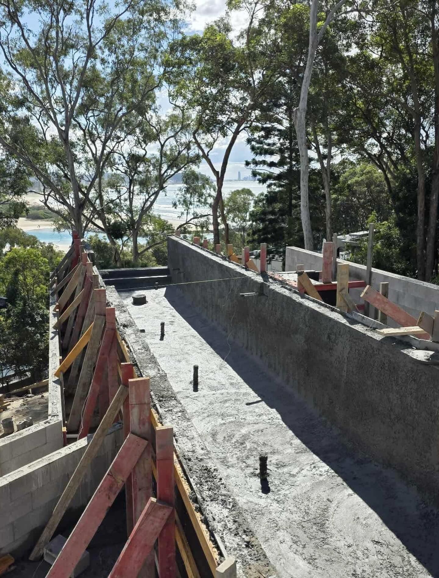 Concrete construction site overlooking trees and a body of water, supported by wooden frames.
