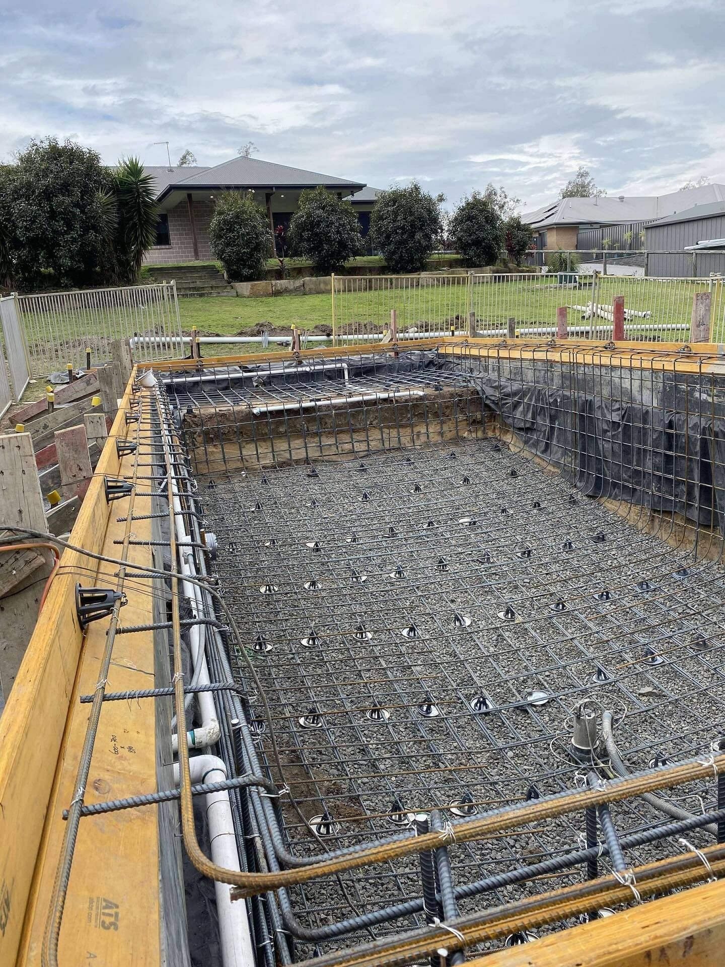 Pool under construction, concrete framework, rebar, filled with gravel, residential setting.