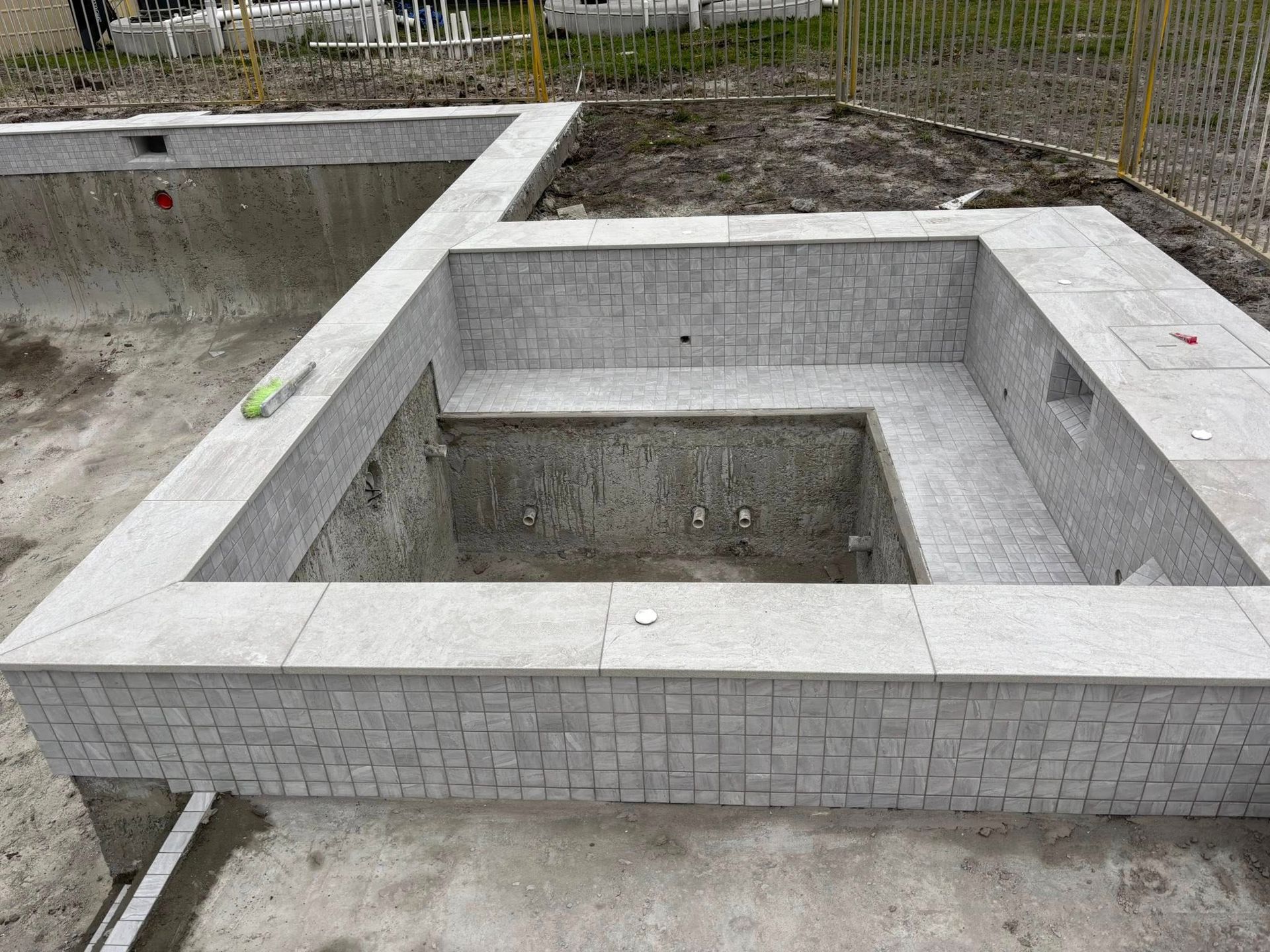 Empty pool with tiled bench seating, in progress, outdoors.