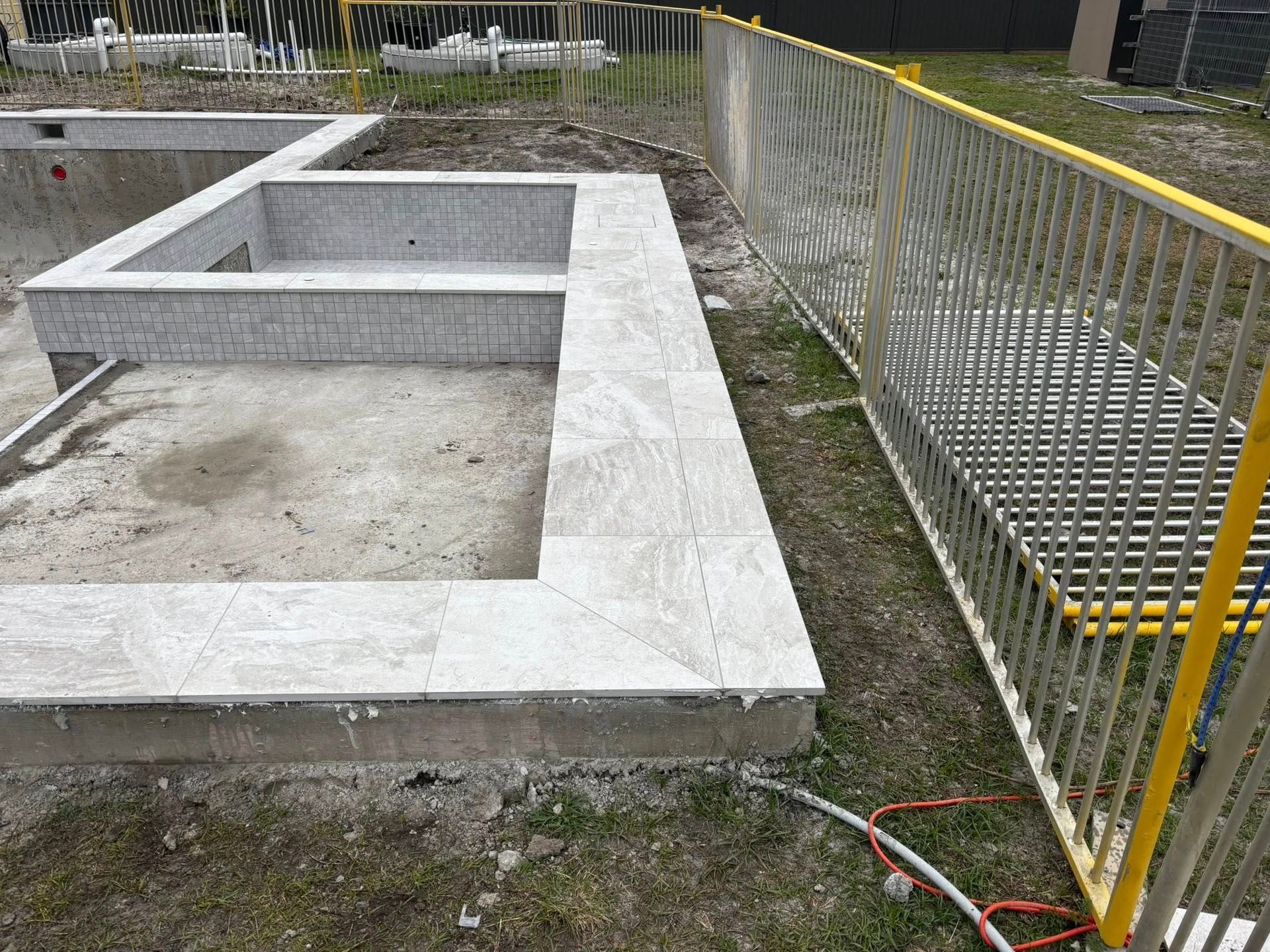 Foundation of a building with a concrete base and gray walls, fenced off with a yellow safety barrier.