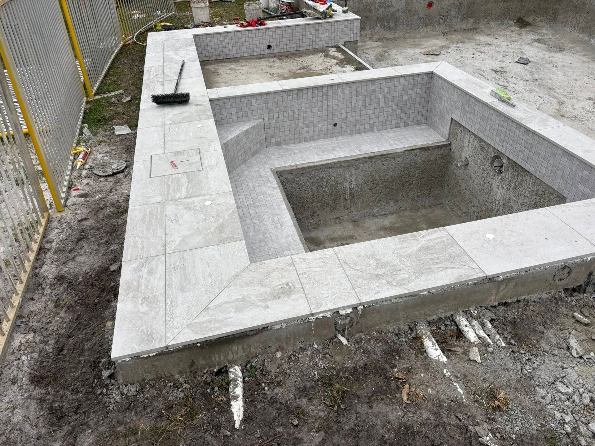 Pool under construction; gray stone edging and steps, concrete basin.