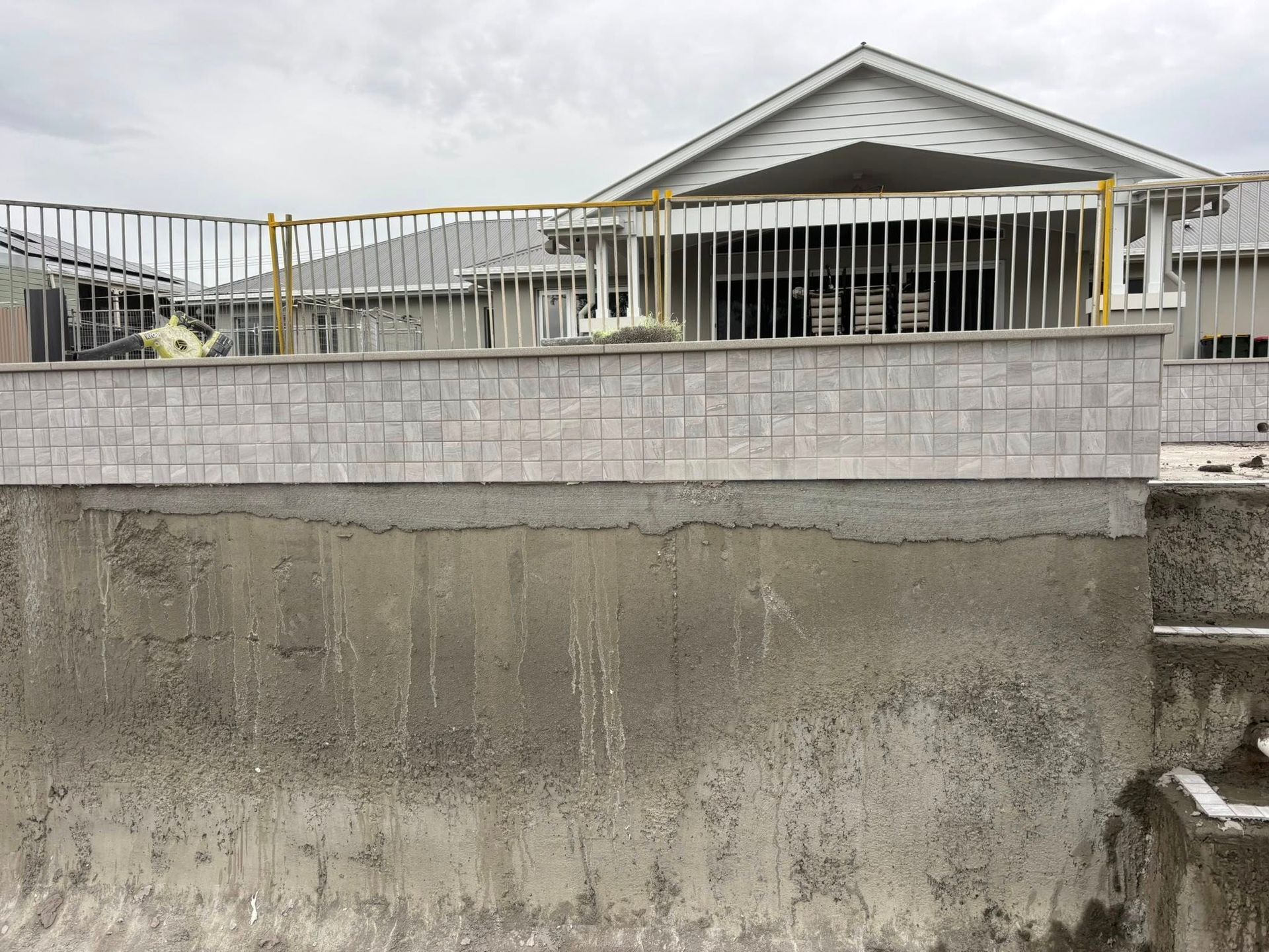 Concrete wall and fence border a home with a gray roof under a cloudy sky.