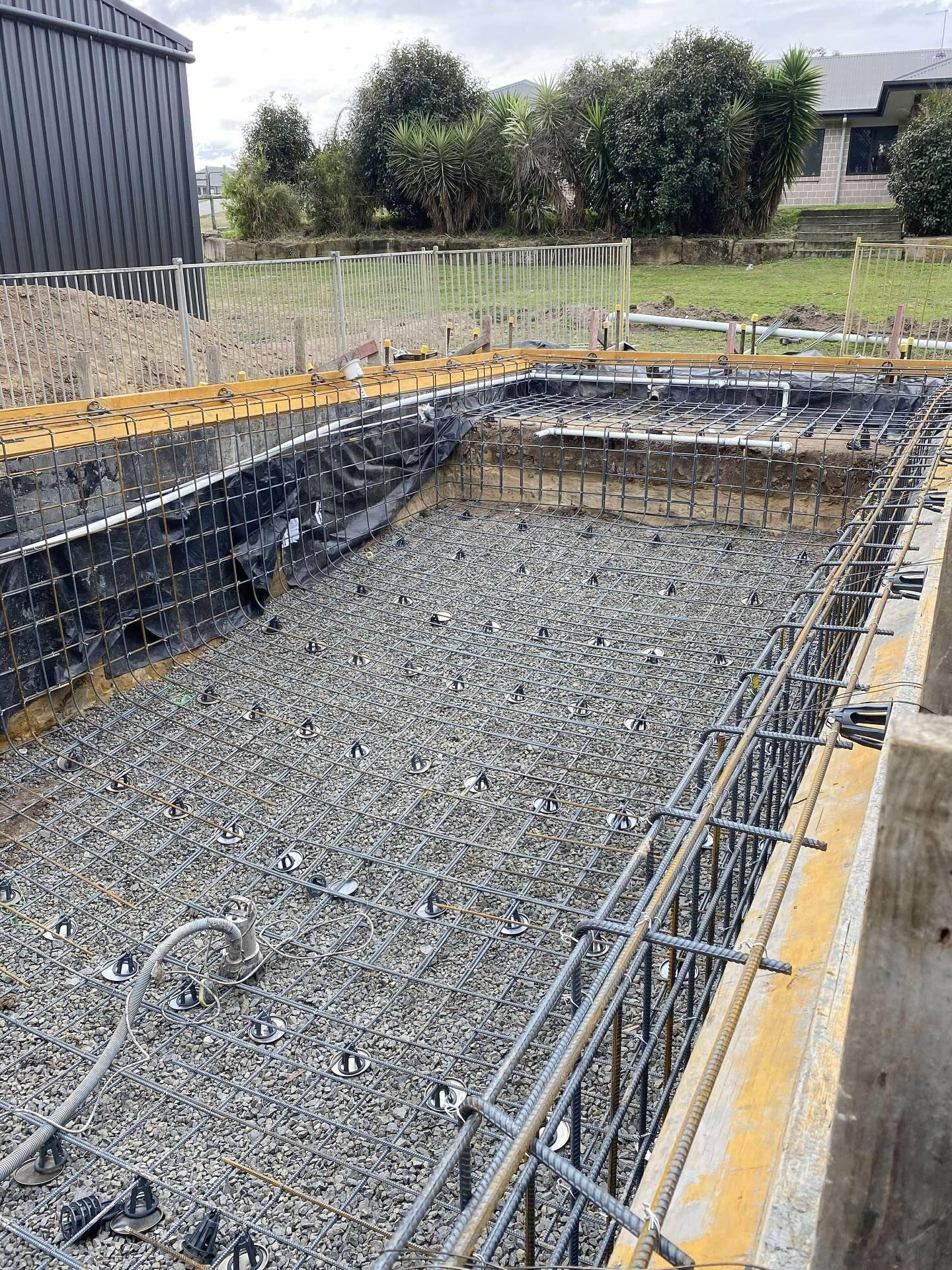 Pool construction site with gravel base, steel reinforcement, and prepared walls.