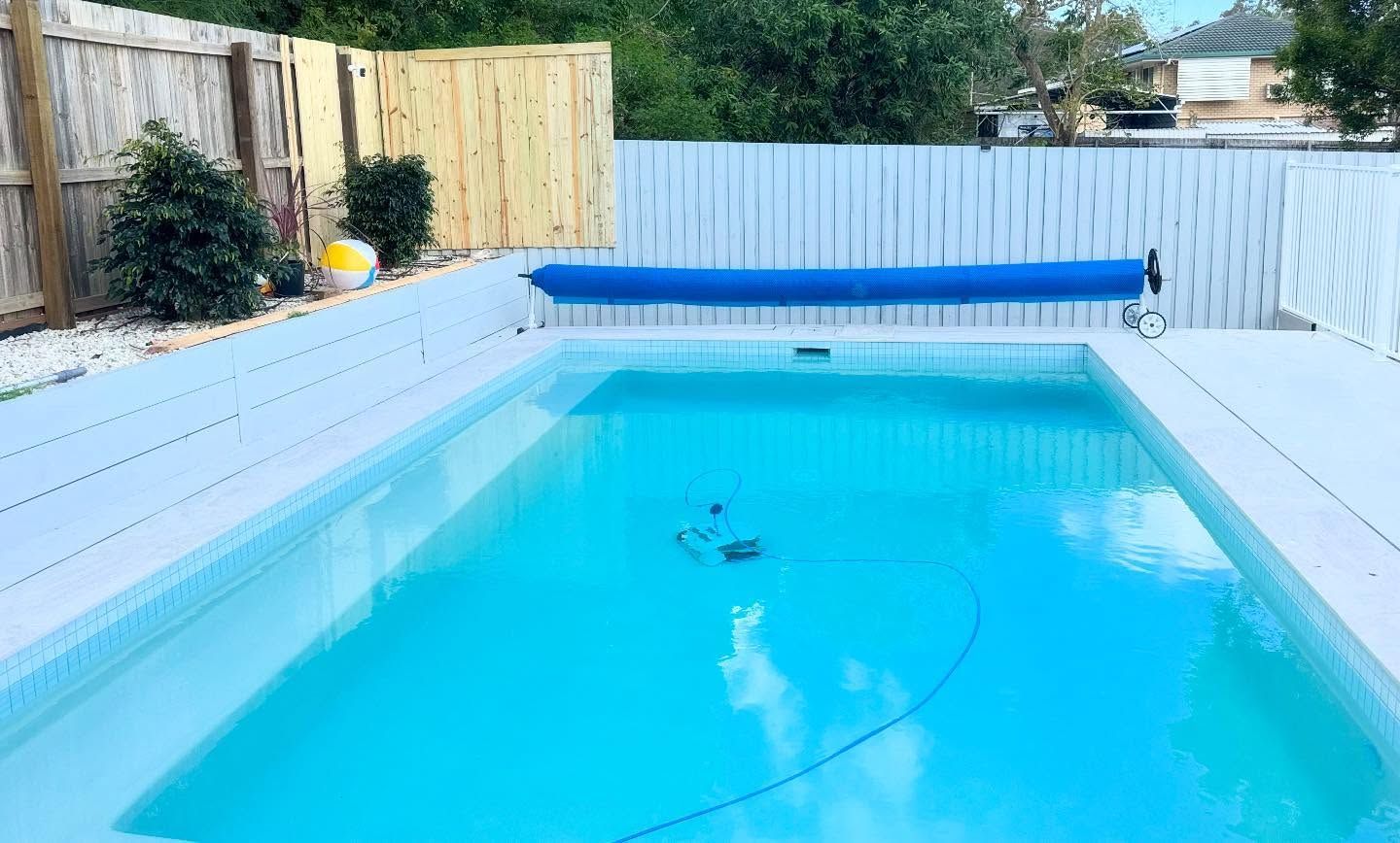 Rectangular outdoor pool with light blue water, white deck, and a blue cover.