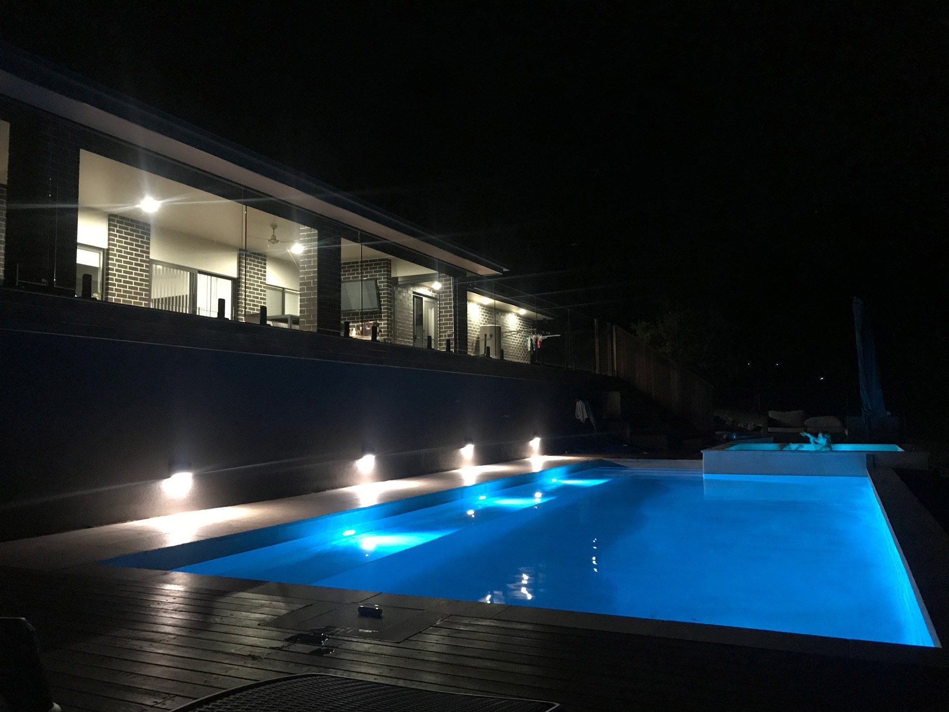 A modern house with a blue illuminated pool at night. Lights shine from the house and in the pool.