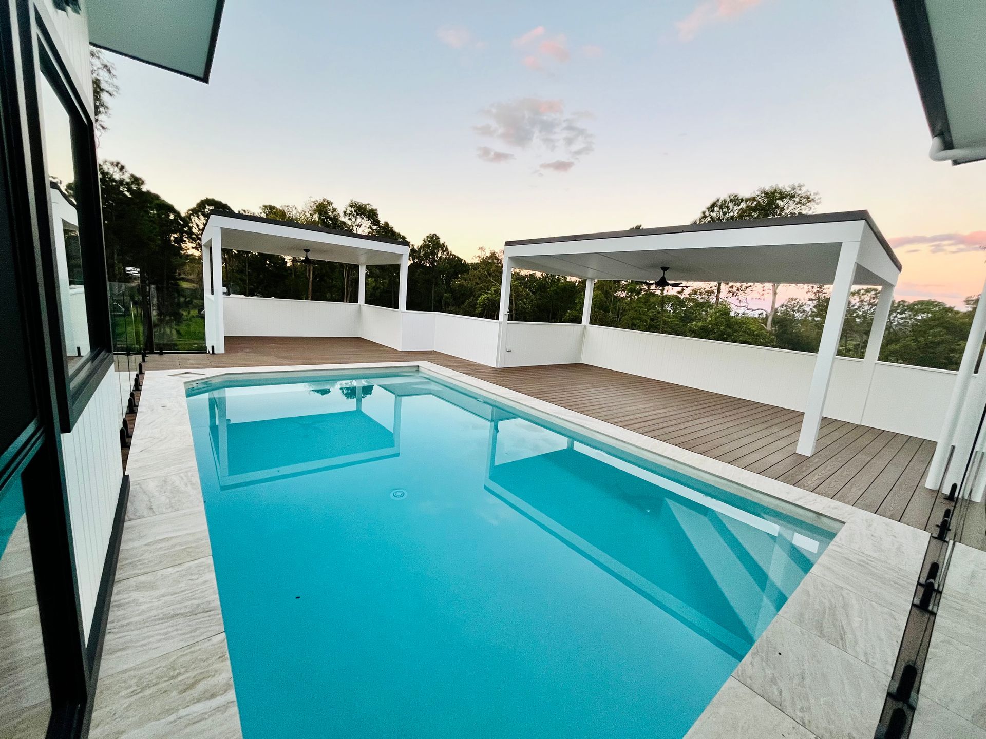 Swimming pool with two white pergolas, composite decking, and a colorful sunset.