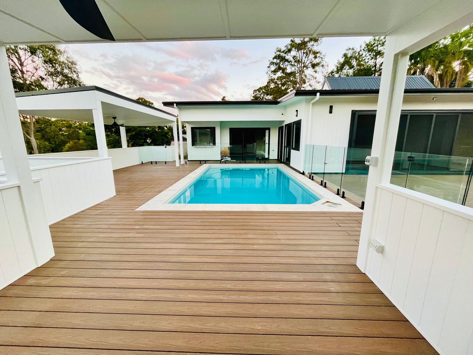 Wooden deck with pool and white house in background.