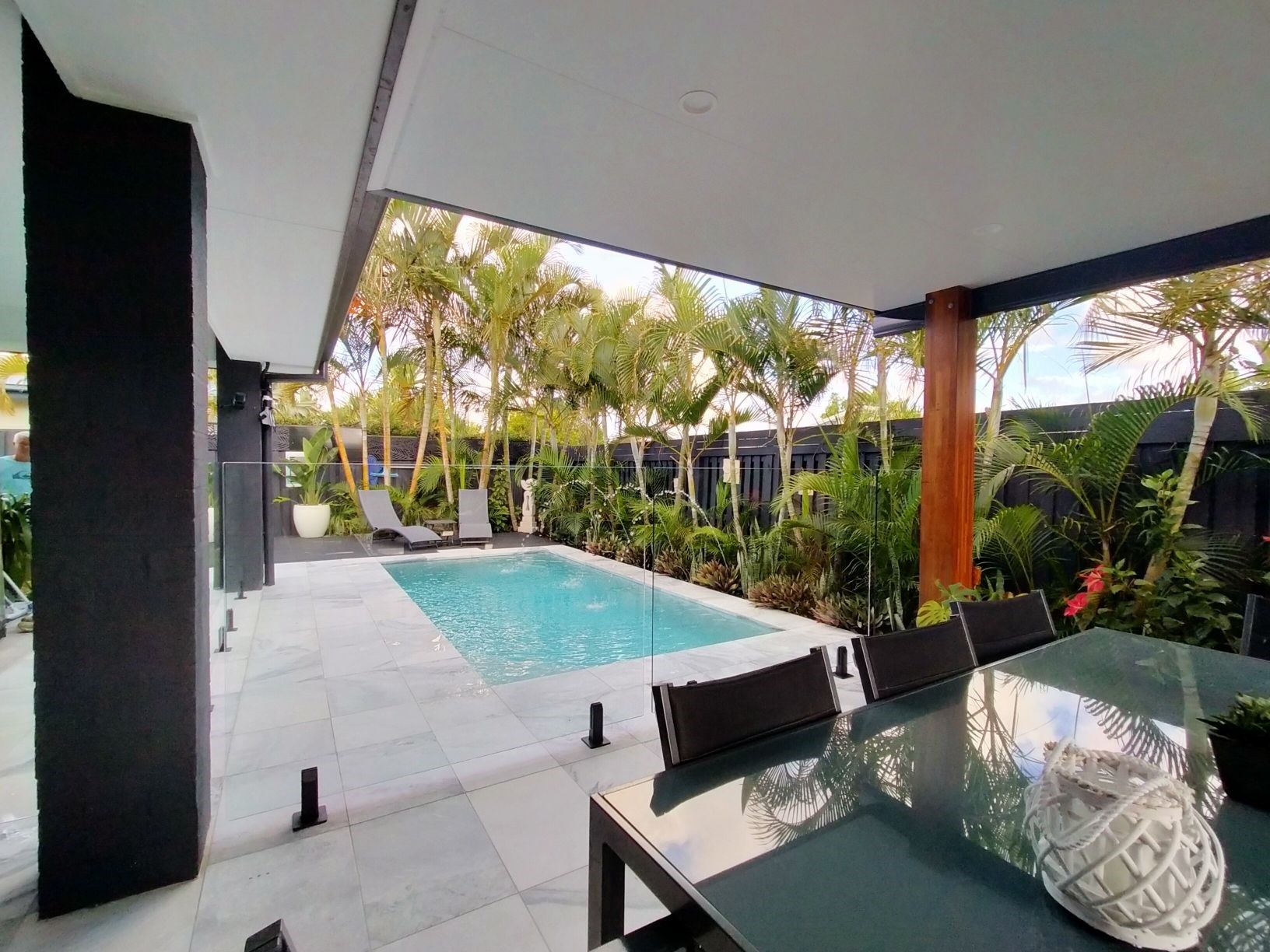 Poolside patio with a dining table, pool, and lush tropical foliage.