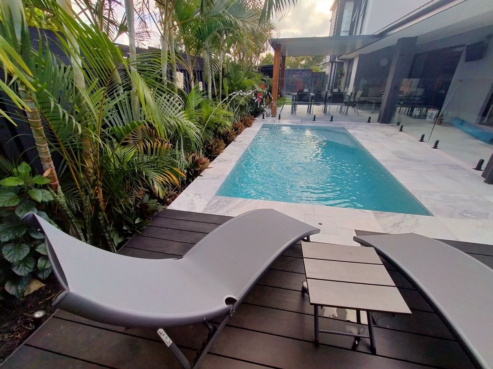 Pool with lounge chairs, surrounded by greenery and modern architecture.