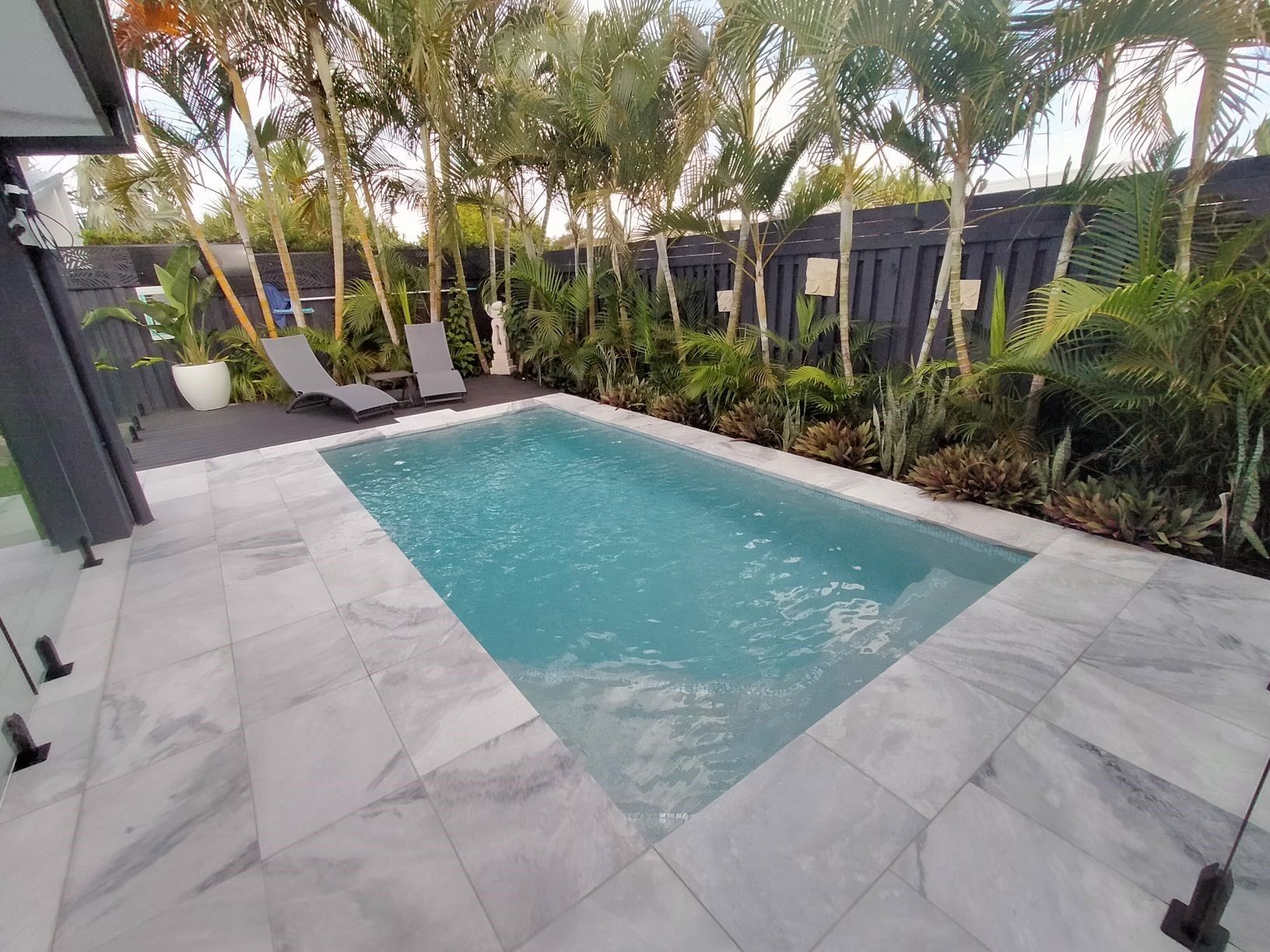 Small rectangular pool surrounded by marble tiles, with lounge chairs in a tropical setting.