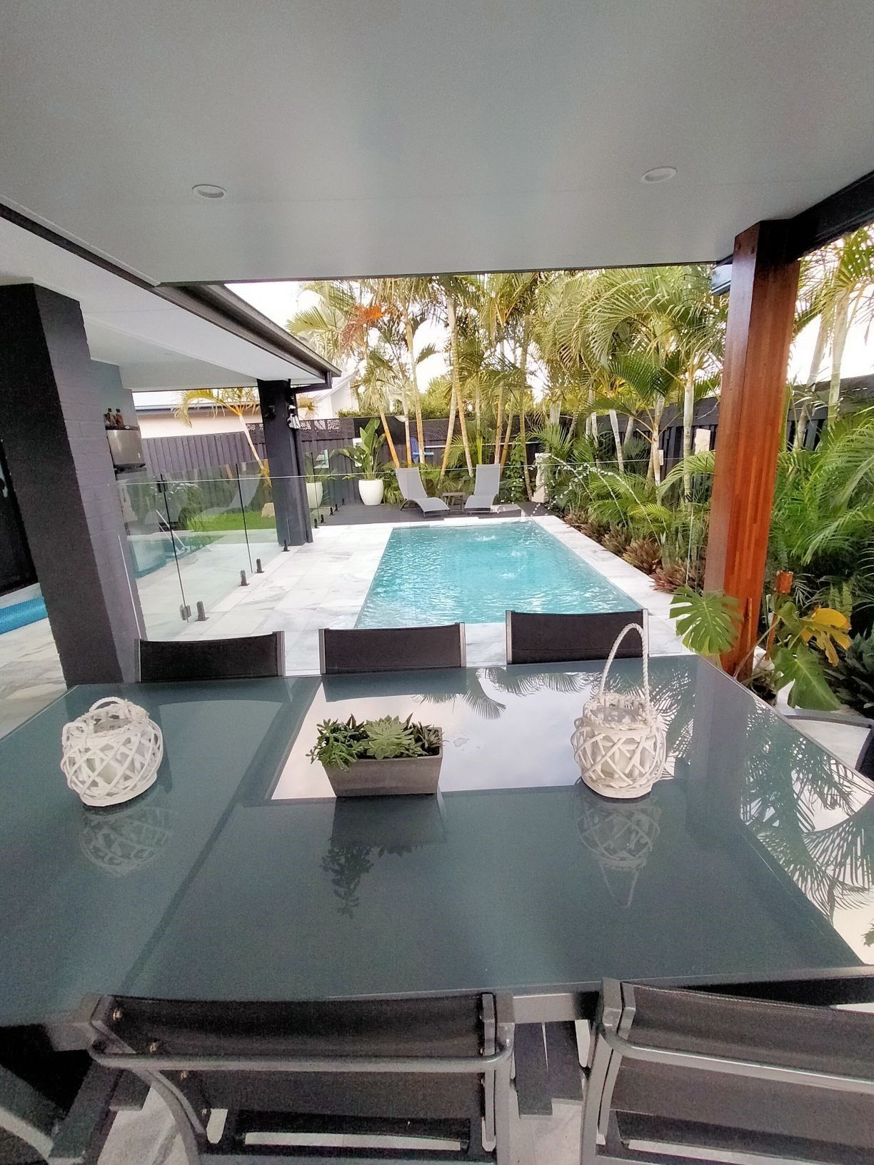Patio table with view of a pool, lush landscaping, and modern home.