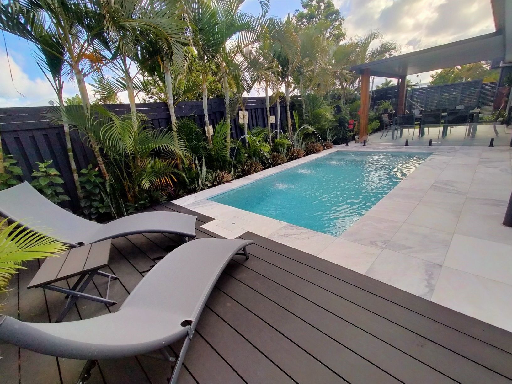 Pool and deck area with lounge chairs, palm trees, and a dark pergola.