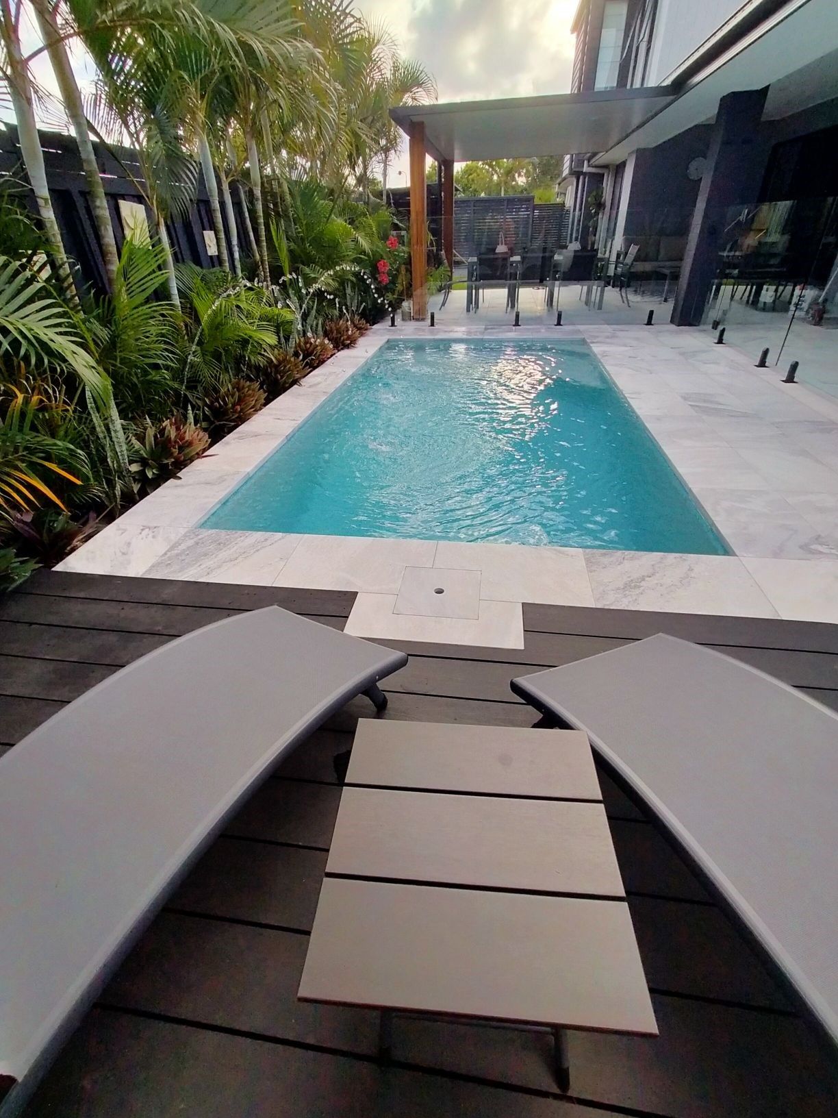 Pool area with lounge chairs, a rectangular pool, and tropical plants.