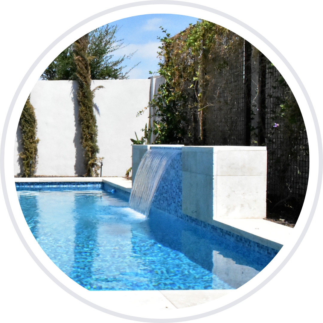Pool with blue mosaic tile and waterfall feature, surrounded by white walls and greenery.