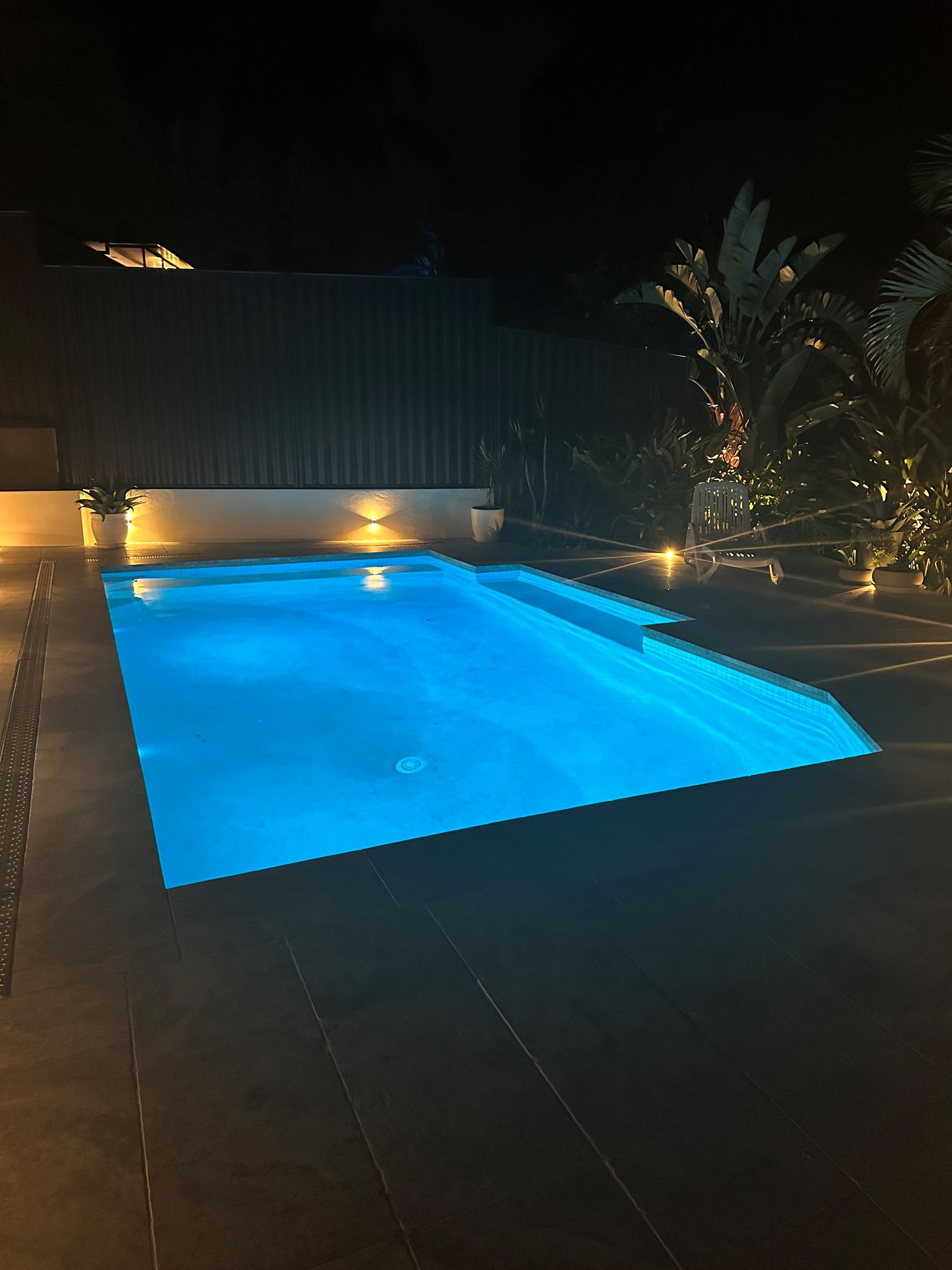 Pool illuminated at night with blue water and surrounding patio.