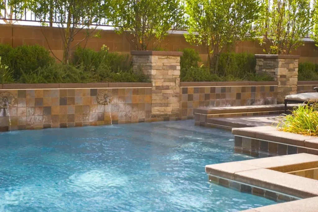Swimming pool with cascading water feature and lush greenery.