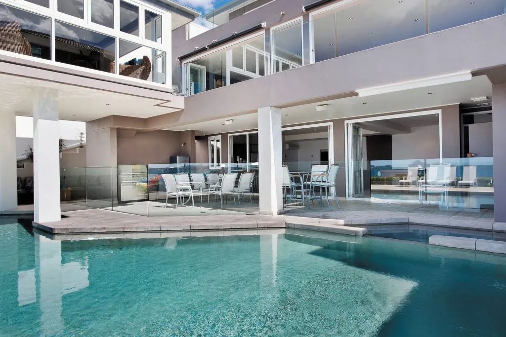 Luxurious home with pool; teal water, modern architecture, outdoor dining area.