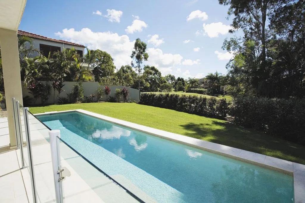 Long, rectangular pool next to a lawn, trees in the background, bright sunlight.