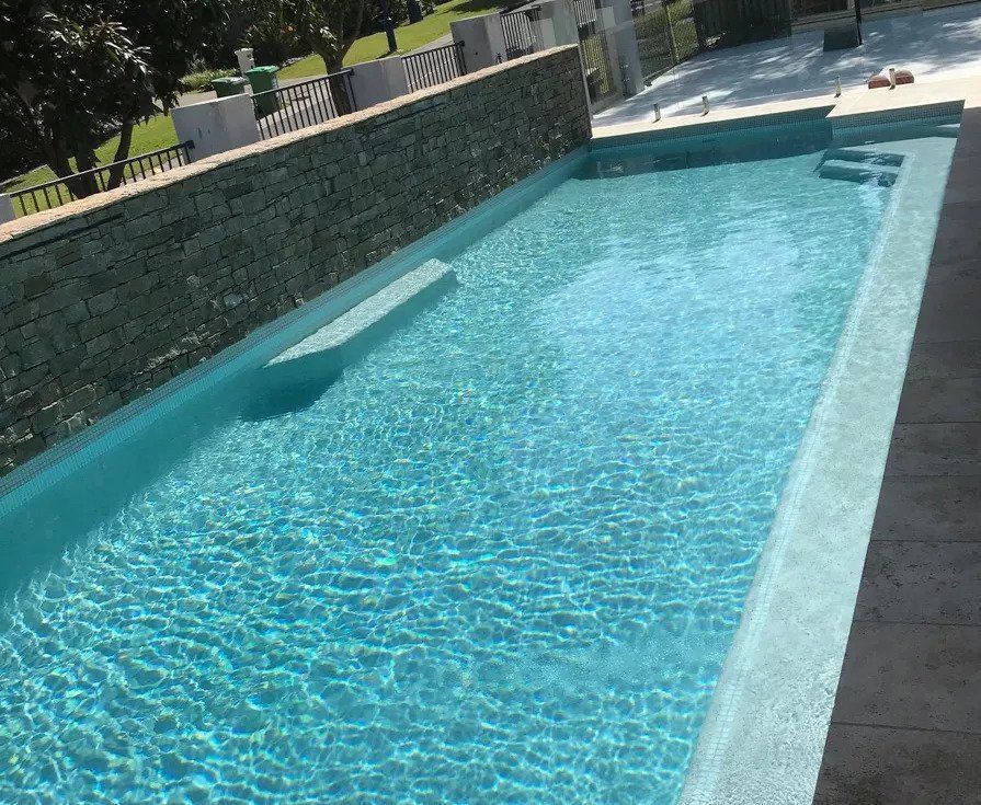 Rectangular swimming pool with turquoise water, stone surround, and a textured stone wall.