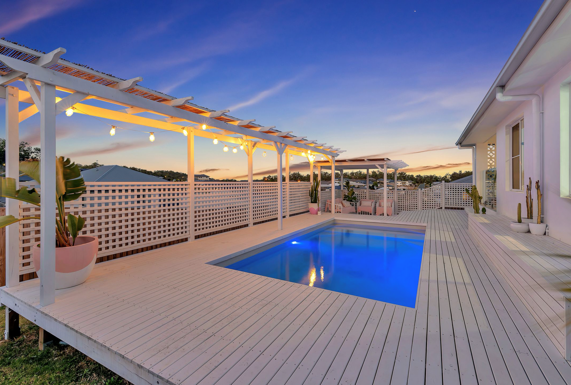 White deck and pool at dusk, string lights on pergola.
