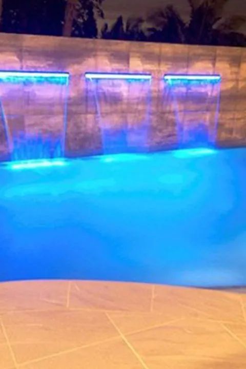 Blue-lit swimming pool with three waterfalls cascading into the water.
