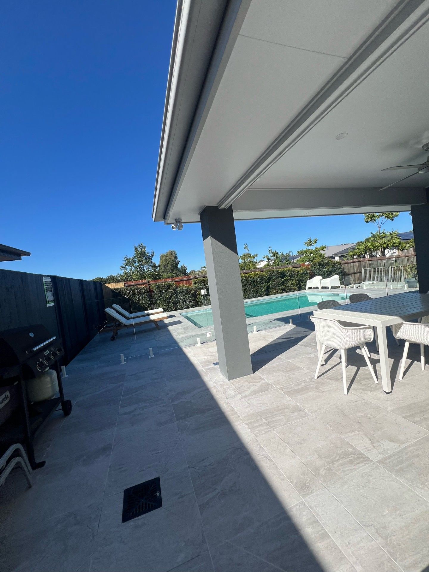 Patio with pool. Gray patio tiles, outdoor furniture, swimming pool under a clear blue sky.