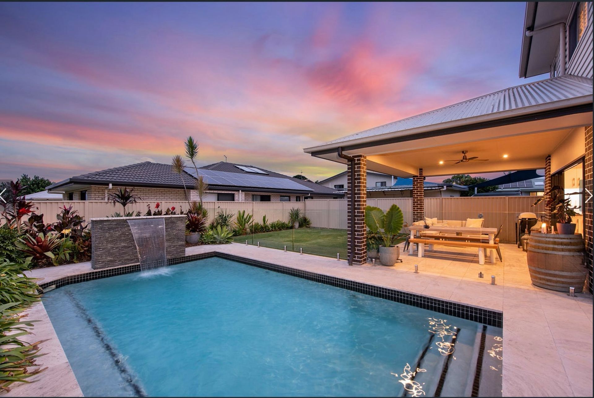 Swimming pool with a water feature and covered patio at sunset.