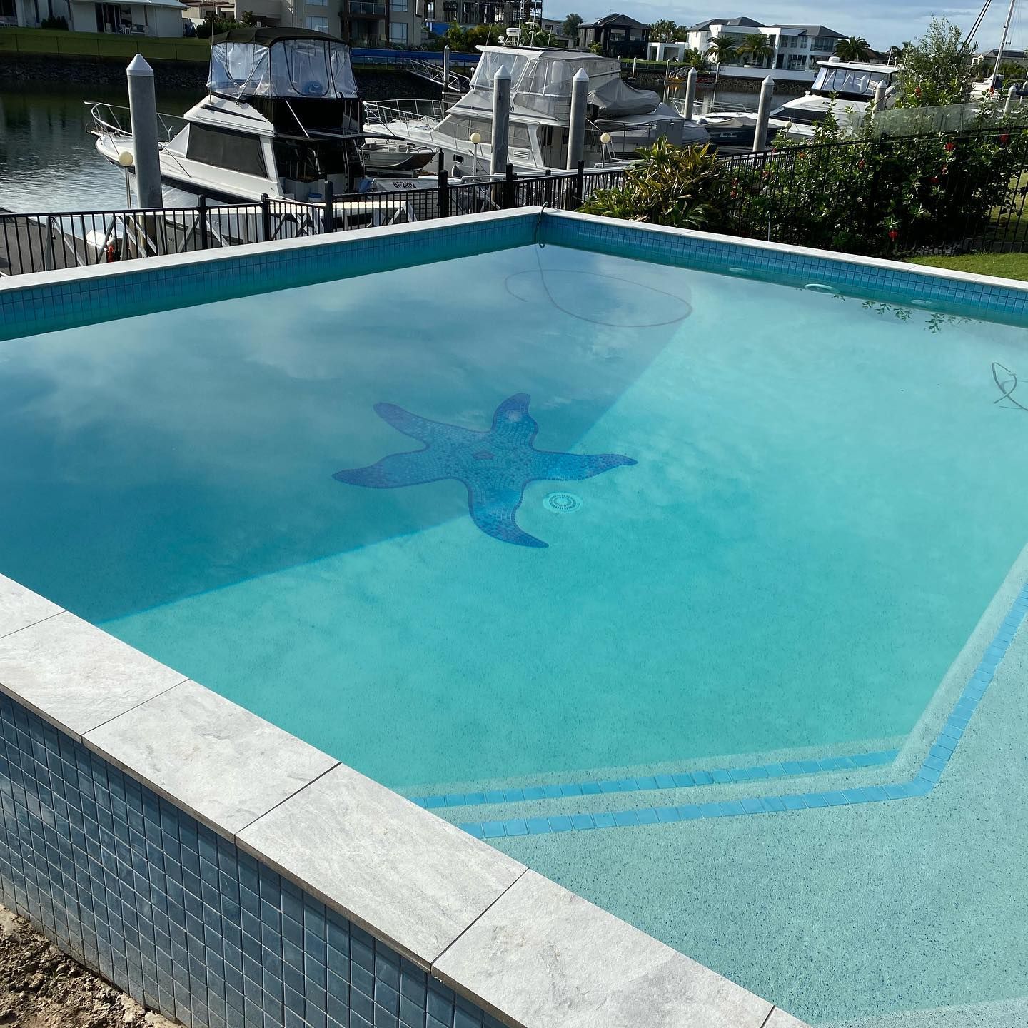 Square swimming pool with a blue starfish mosaic on the bottom, near a dock with boats.
