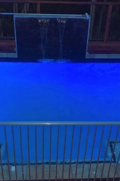 Pool with blue water illuminated by blue lights, with a small waterfall feature.