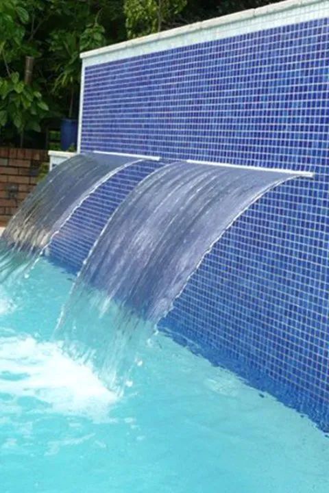 Blue tiled pool wall with three waterfall features pouring into the turquoise water.