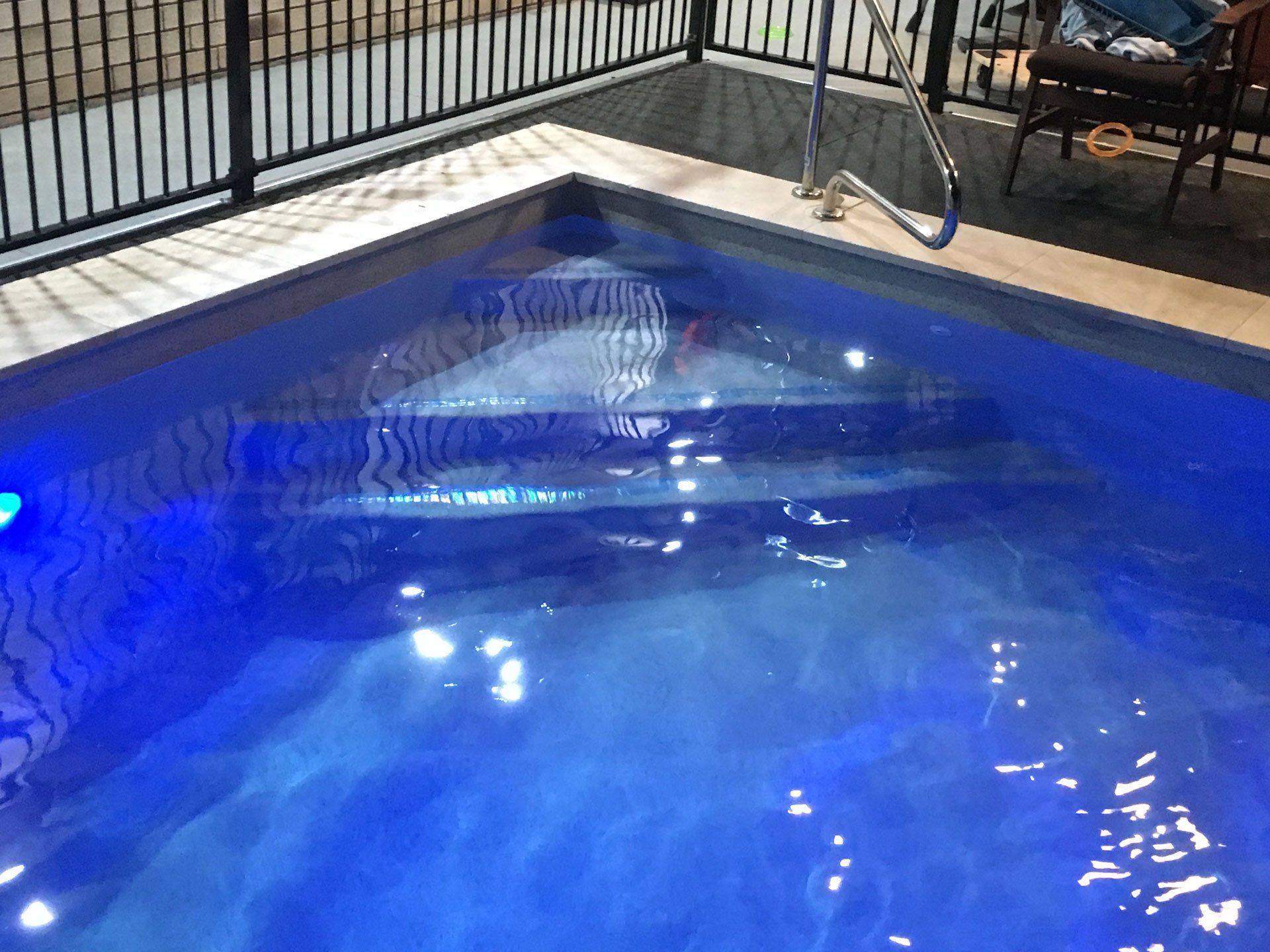 Blue pool with steps, metal fence, and a ladder. Water shimmering.