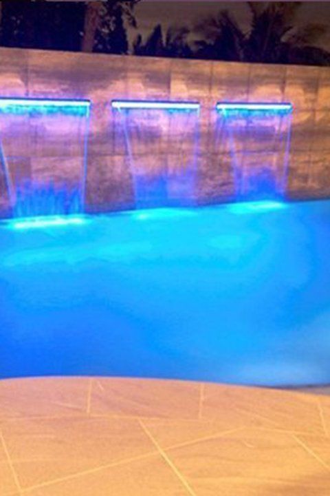 Blue-lit pool with three waterfalls, nighttime setting.