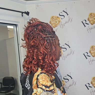A woman with red hair is standing in front of a wall that says sy braids
