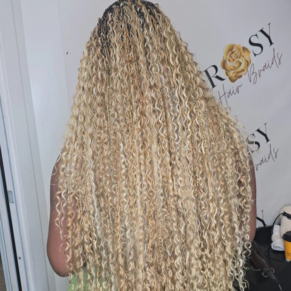A woman with very long blonde curly hair is standing in front of a sign that says rosy