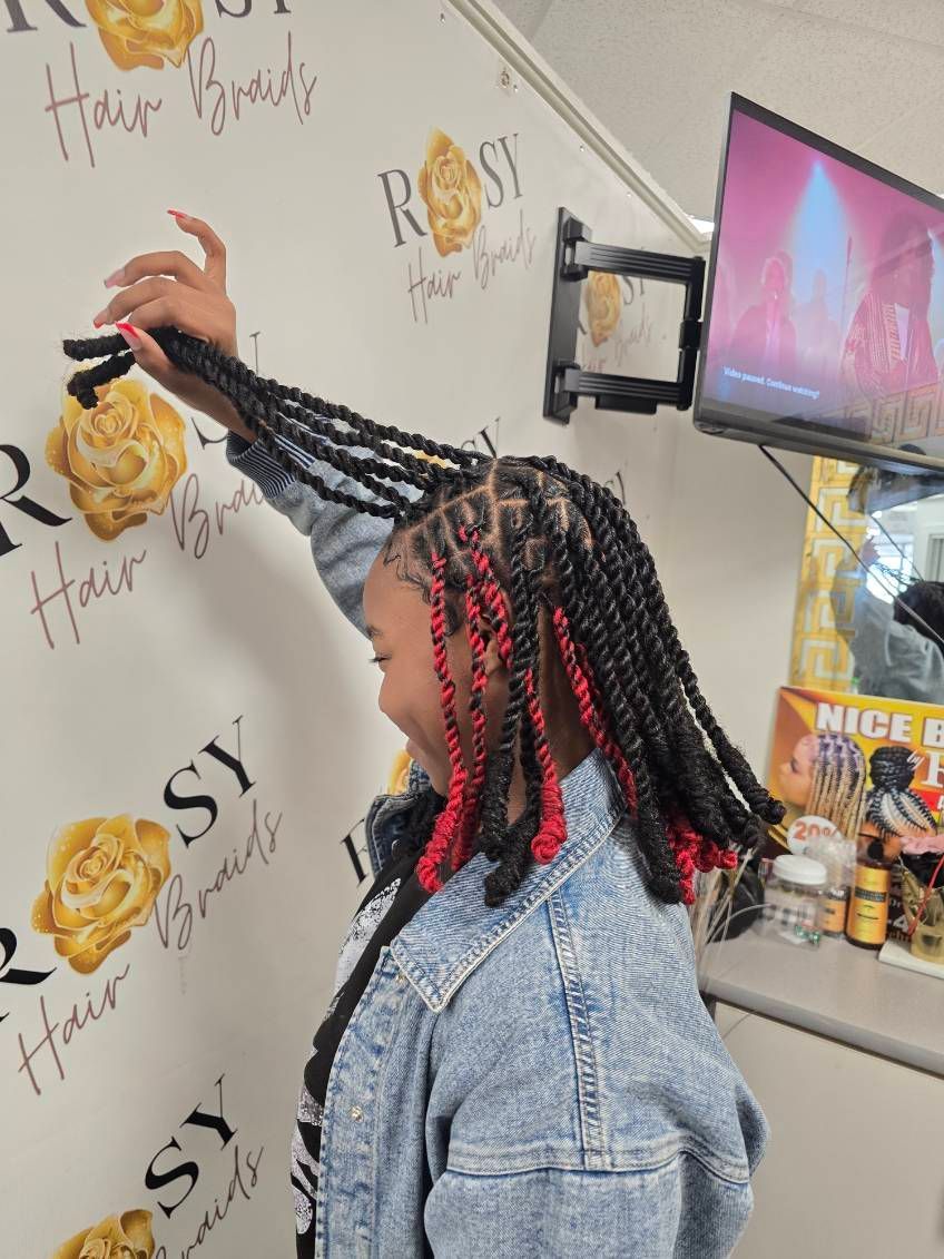 A woman with braids is sitting in a chair in front of a wall that says rossy