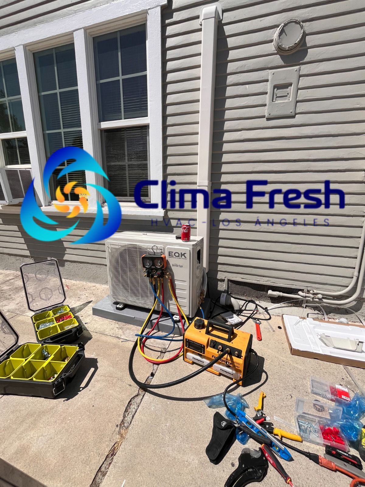 A man is standing on a ladder fixing an air conditioner on the side of a building.