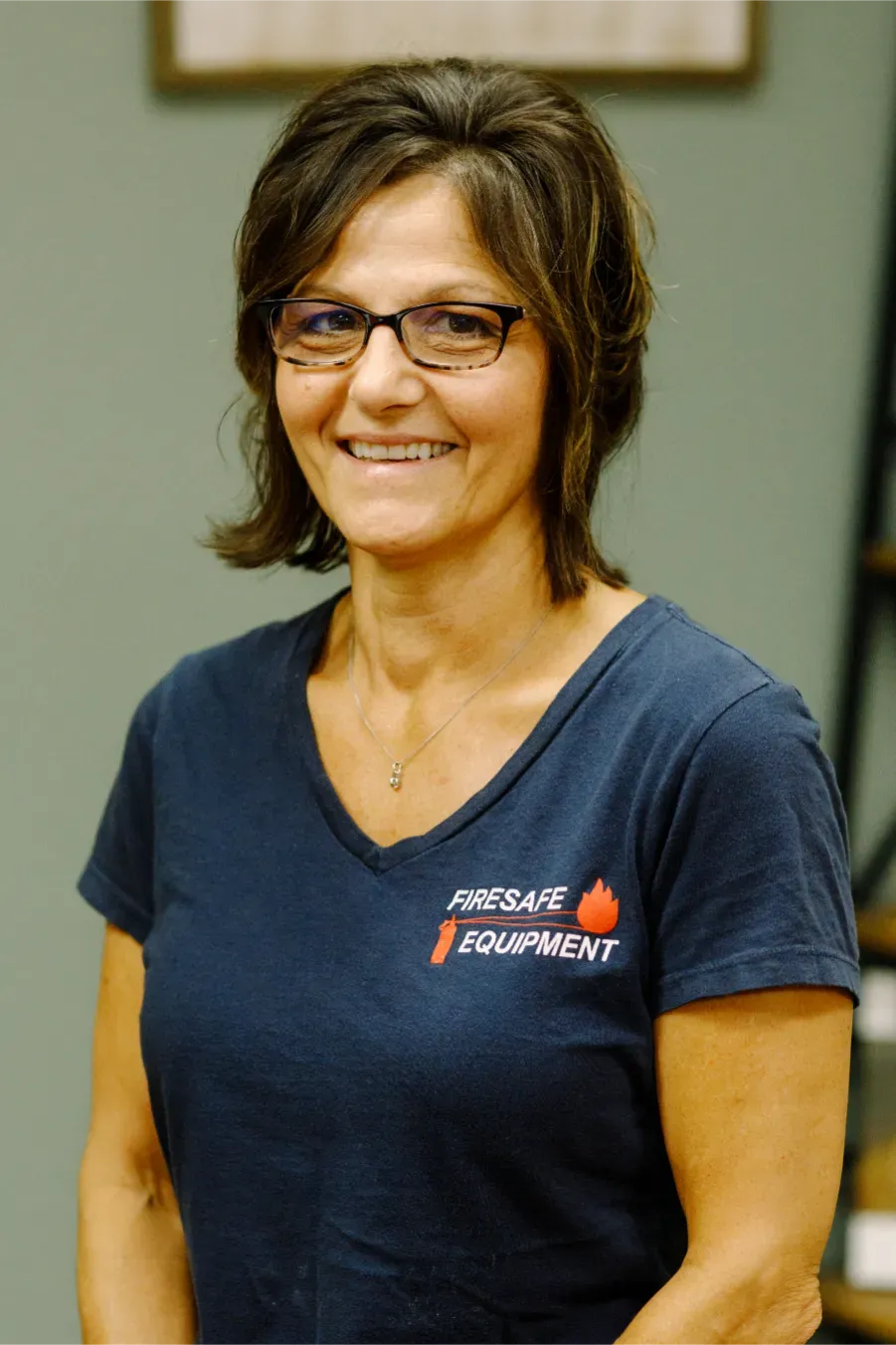 A woman wearing glasses and a blue shirt is smiling for the camera.