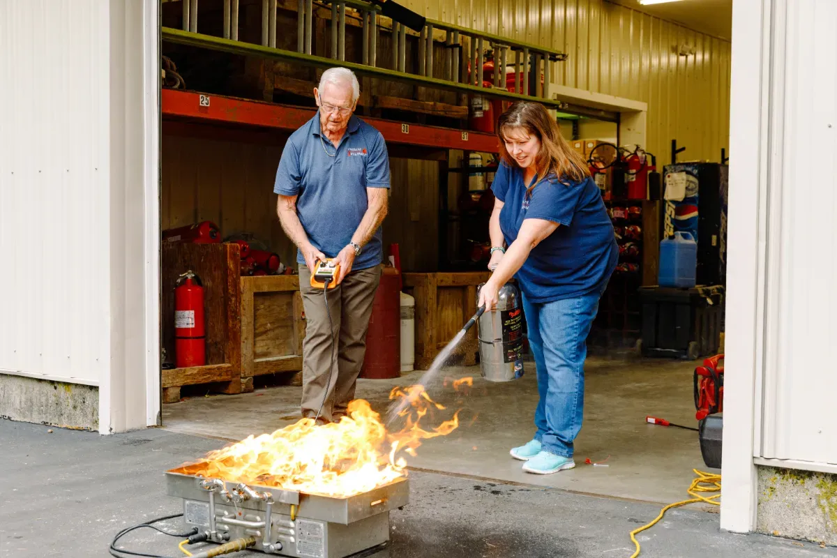 A man and a woman are using a fire extinguisher to put out a fire.