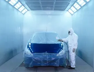 A man is painting a blue car in a paint booth.