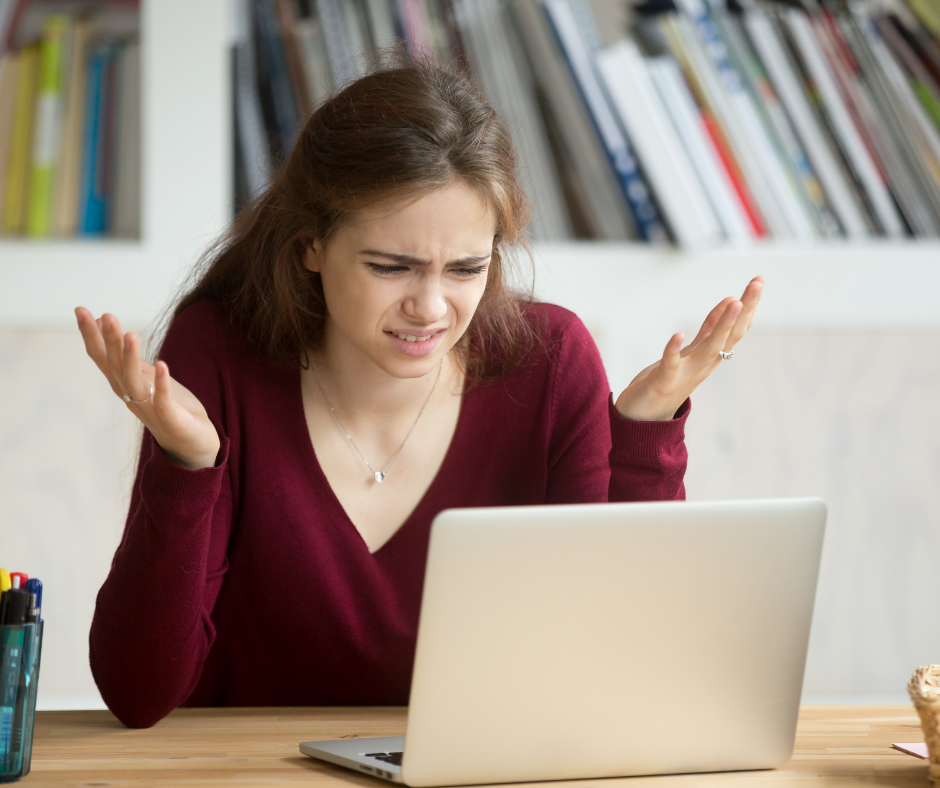 Young adult female looking at computer with hands up, frustrated