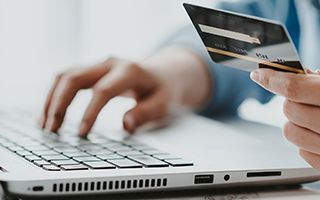Hands typing on a laptop while holding a credit card, suggesting online shopping or payment.