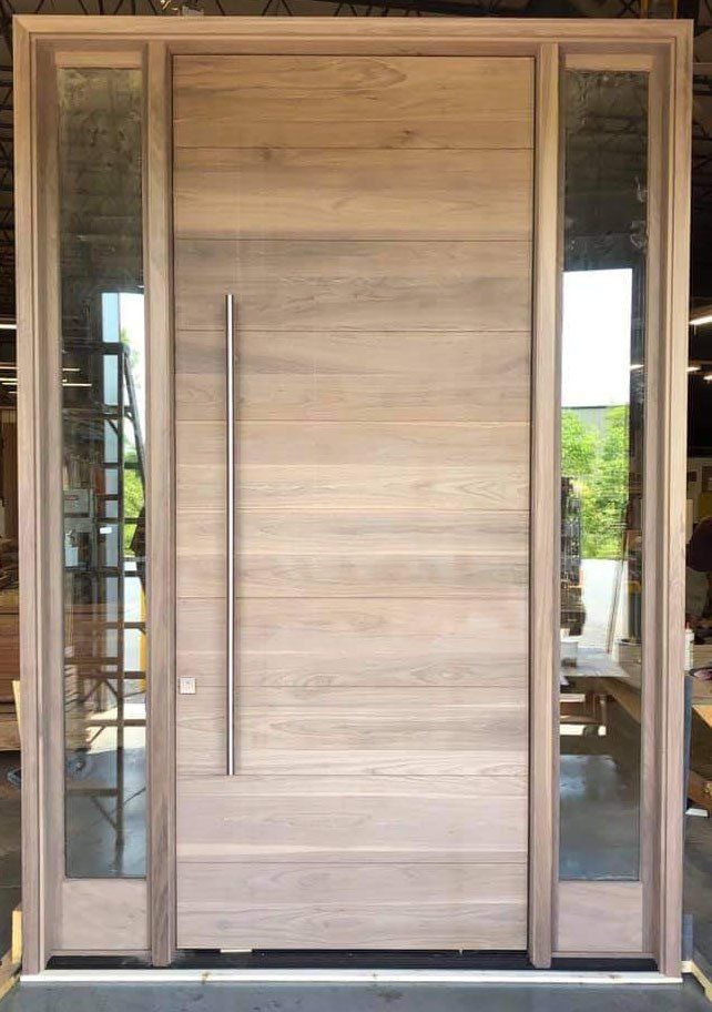 A large wooden door with a stainless steel handle is sitting in a room.