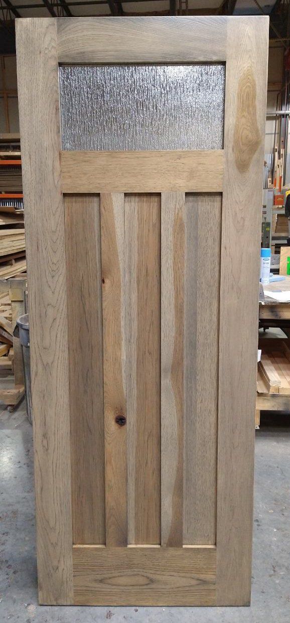 A wooden door with a glass window is sitting on a concrete floor.