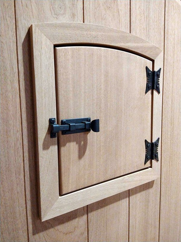 A small wooden door with black hinges on a wooden wall