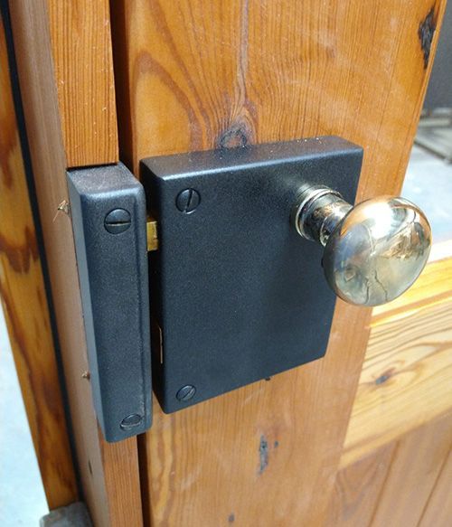 A black door lock with a brass knob on a wooden door
