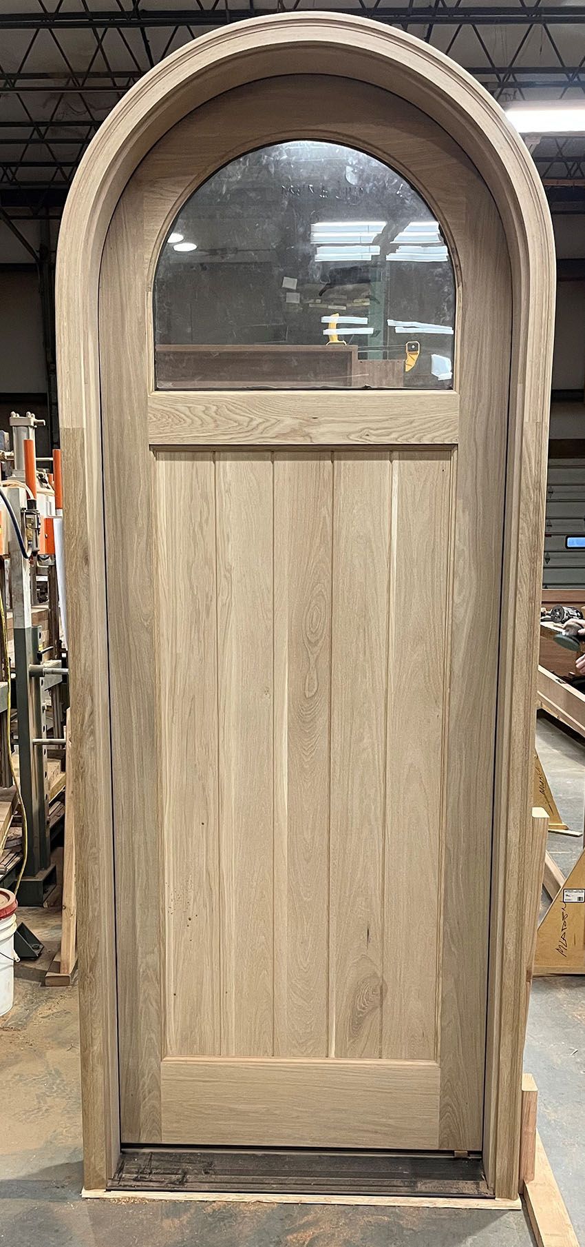 A wooden door with a glass window is being built in a factory.