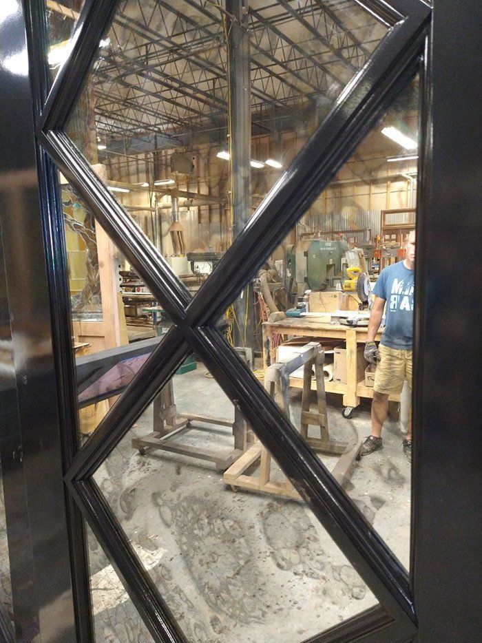 A man in a blue shirt is standing in a workshop behind a glass door.