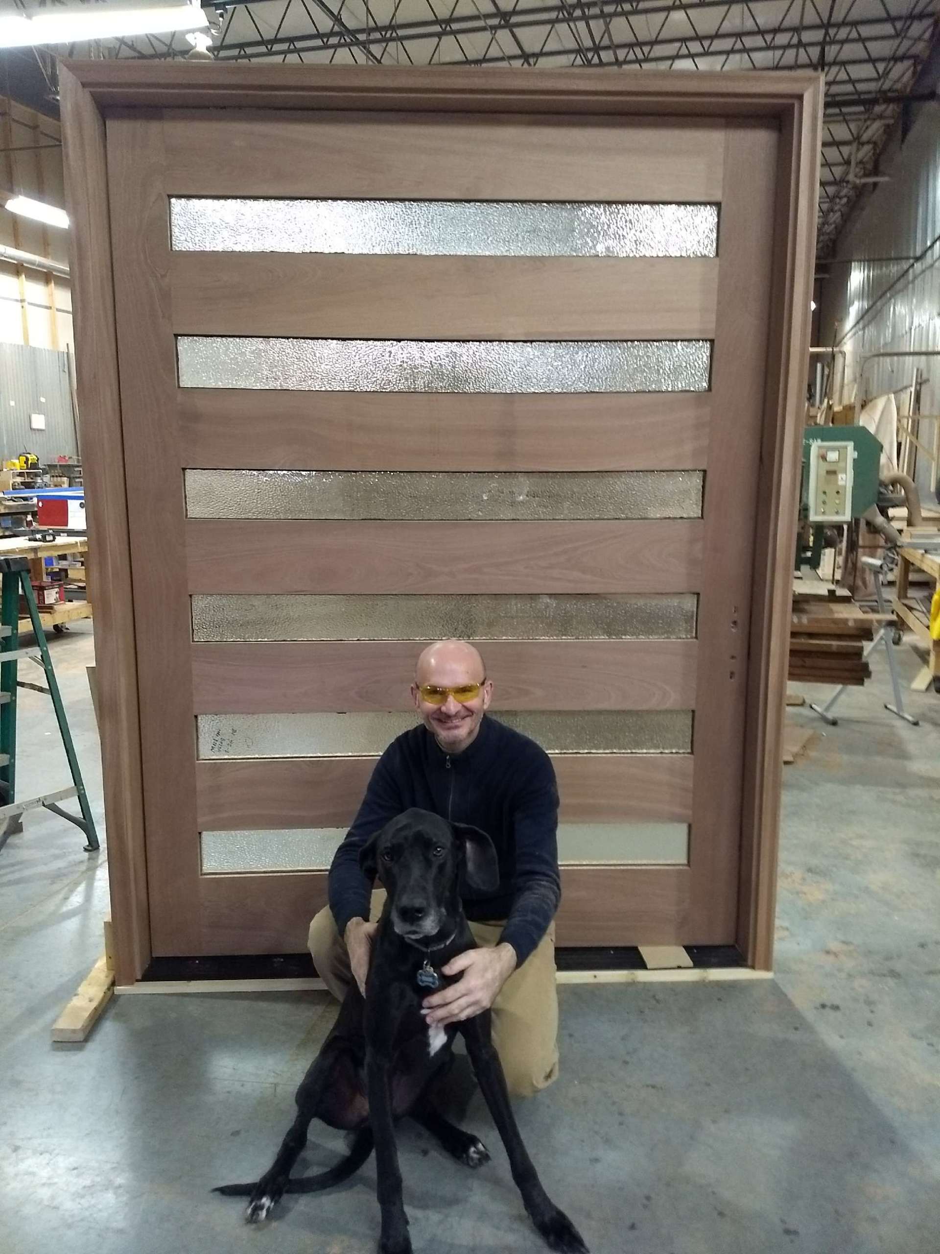 A man is sitting next to a black dog in front of a wooden door.