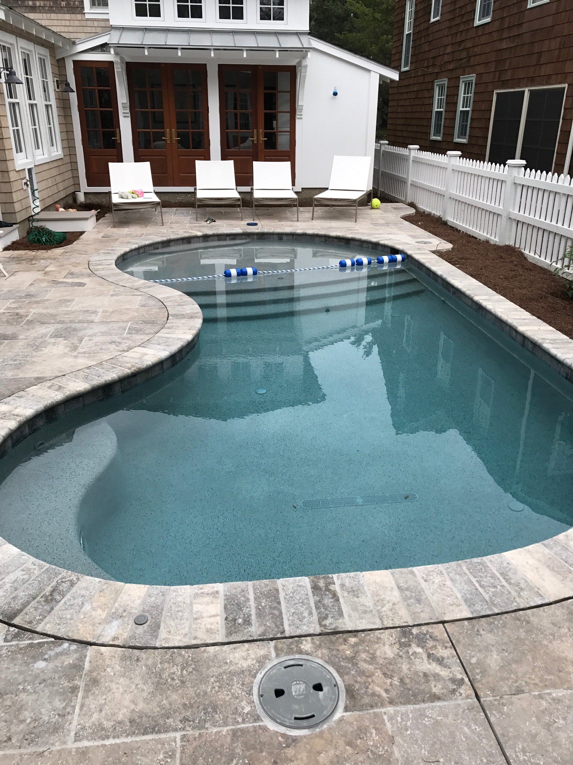 A large swimming pool is surrounded by chairs and a white fence.