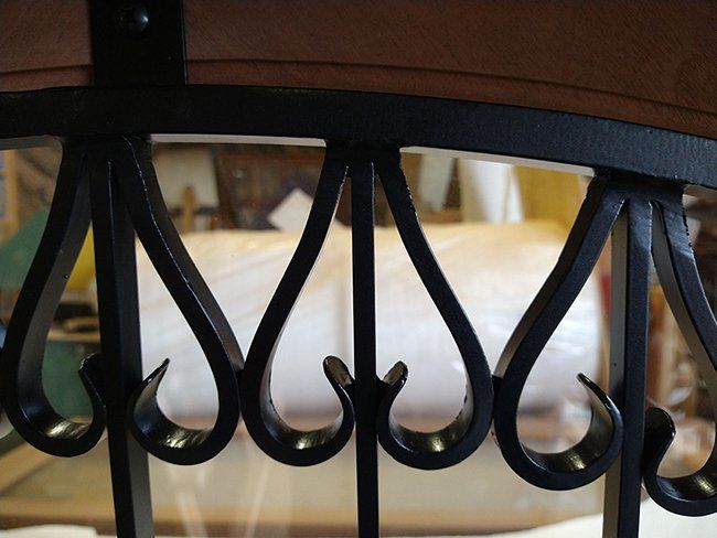 A close up of a wrought iron railing with a bed in the background